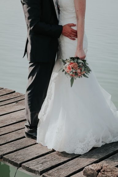 Brud och brudgum står på en brygga, bruden håller en blombukett.