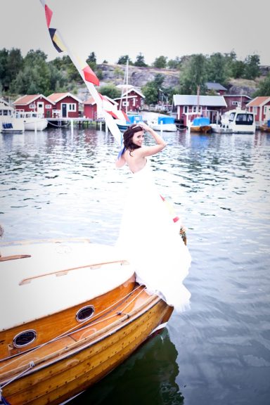 Kvinna i vit bröllopsklänning står på en båt vid en vacker hamn.