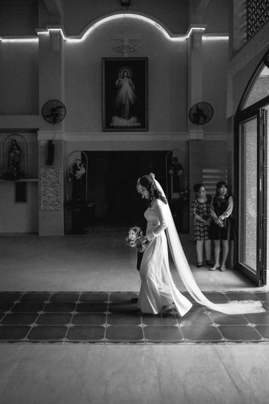 Brud går i en kyrka med en bukett, två kvinnor sitter i bakgrunden.