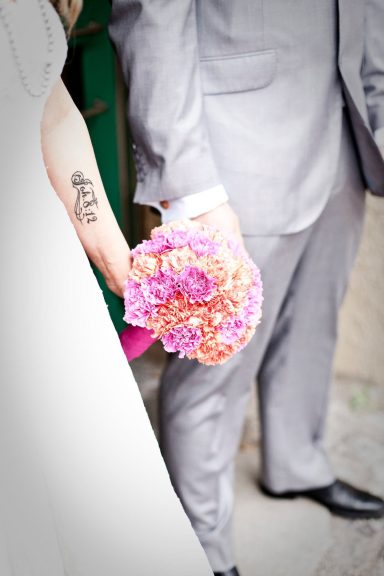 En brud och brudgum håller varandra i handen, bruden har en blommig bukett.